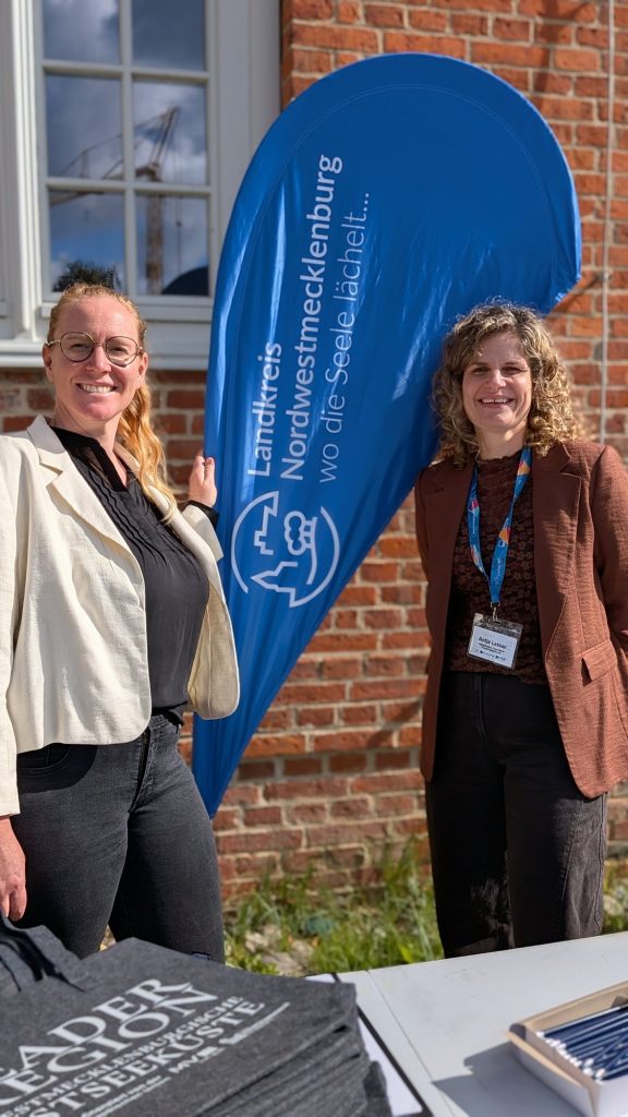 Zwei Frauen am LEADER-Beachflag vor der Backsteinwand von Schloss Plüschow