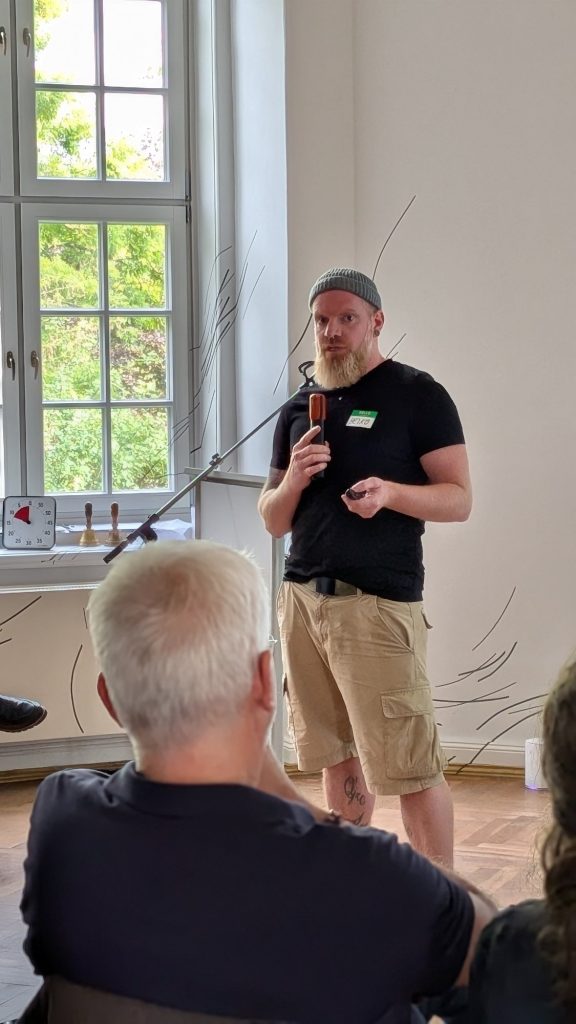 Redner im schwarzen Shirt am Mikrofon vor dem Publikum