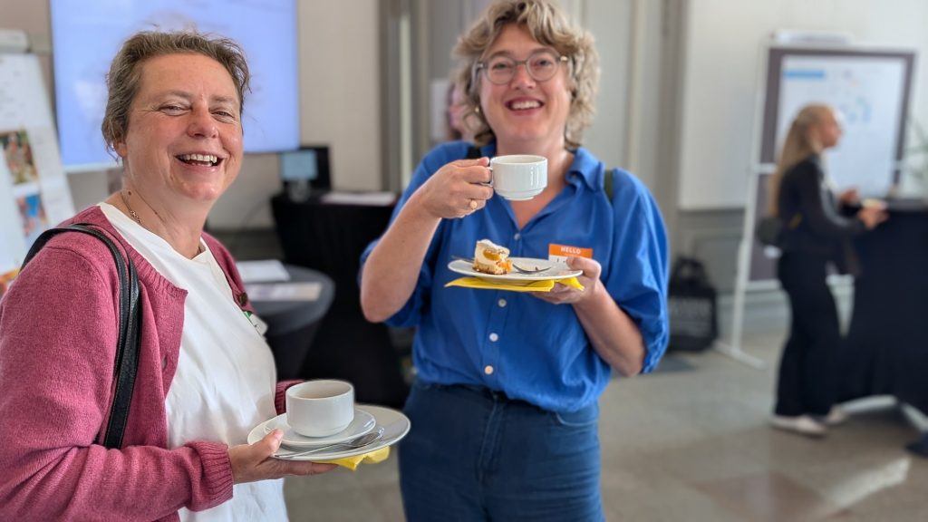 Zwei lachende Teilnehmerinnen mit Kaffee und Kuchen in der Pause