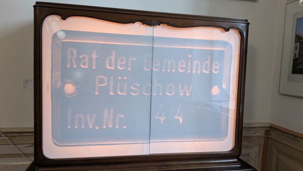 Altes Schild „Rat der Gemeinde Plüschow“ in einer Vitrine