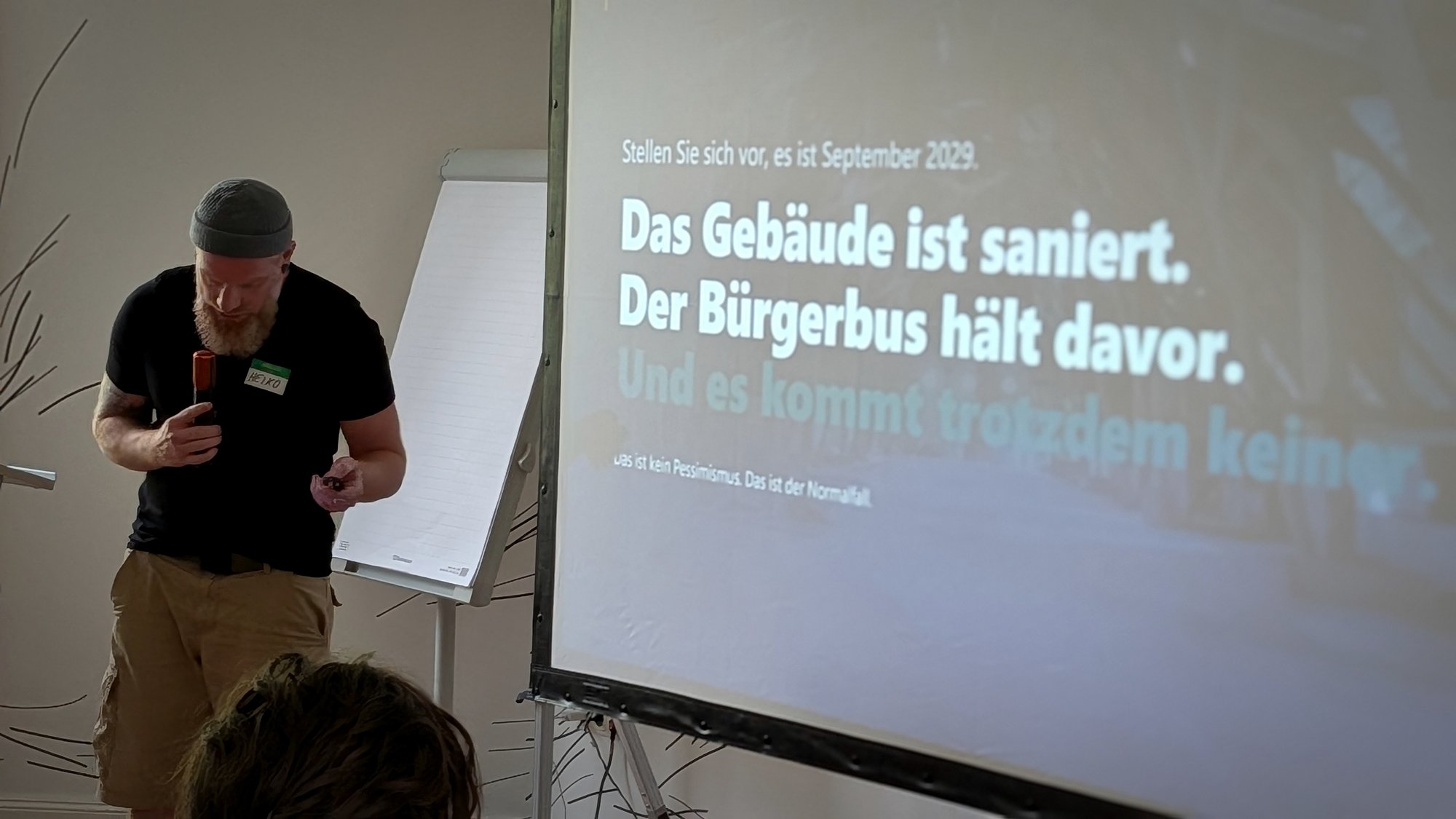 Heiko Kolz vor der Folie: Das Gebäude ist saniert. Der Bürgerbus hält davor. Und es kommt trotzdem keiner.