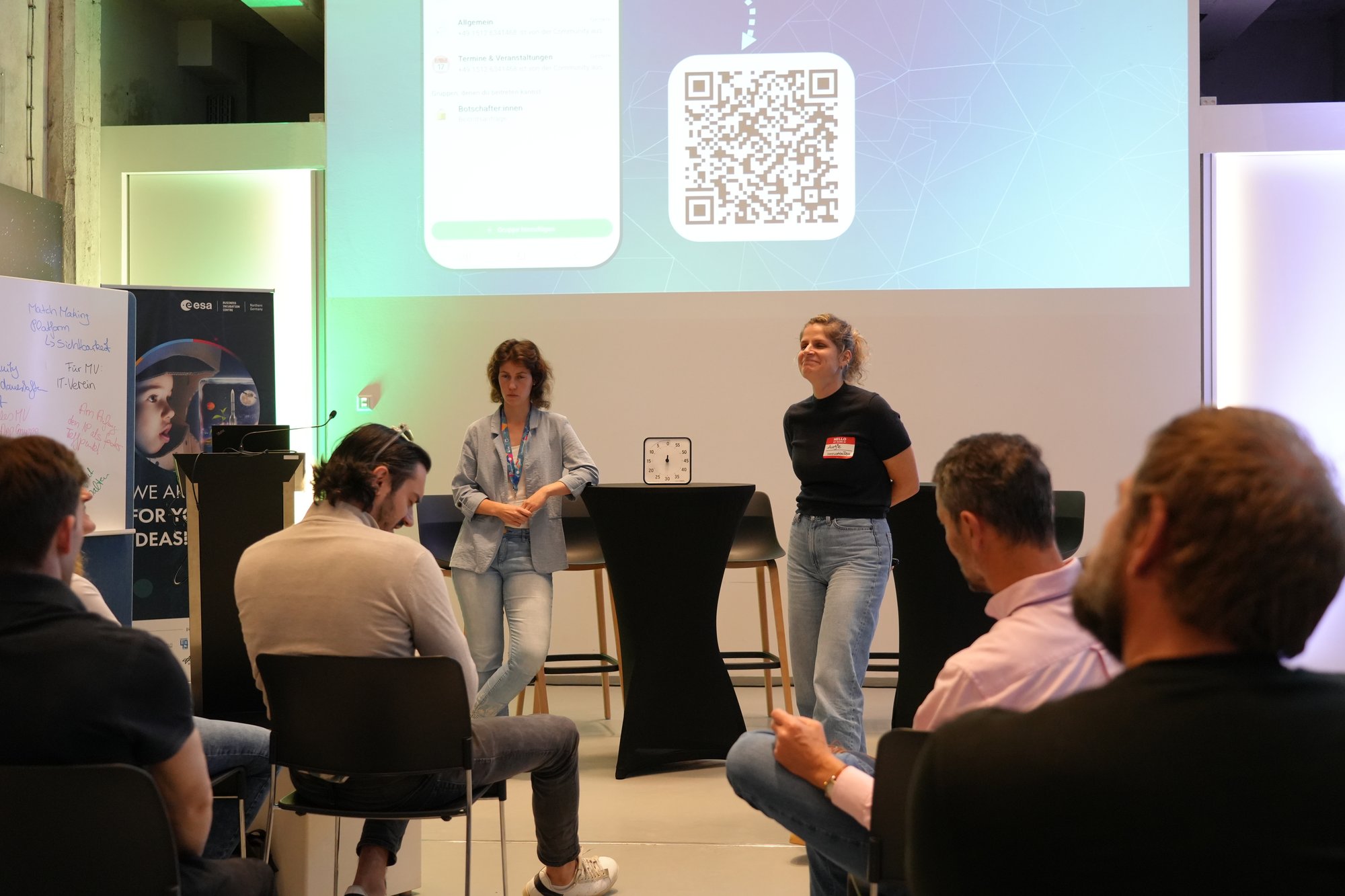 Zwei Moderatorinnen vor der Leinwand mit dem QR-Code zum Beitritt in die WhatsApp-Community