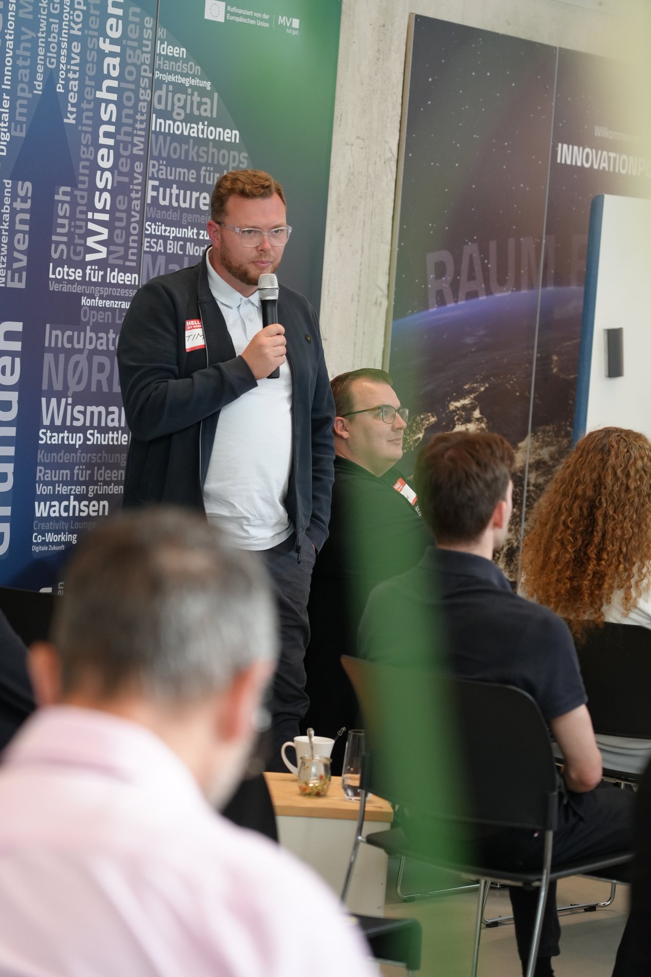 Teilnehmer hält einen Mini-Pitch vor dem Roll-up des Innovation Port