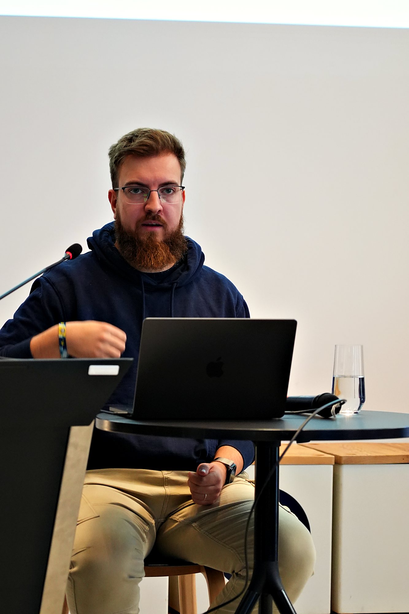Simon Glowik spricht am Stehtisch, vor ihm ein Laptop und ein Wasserglas