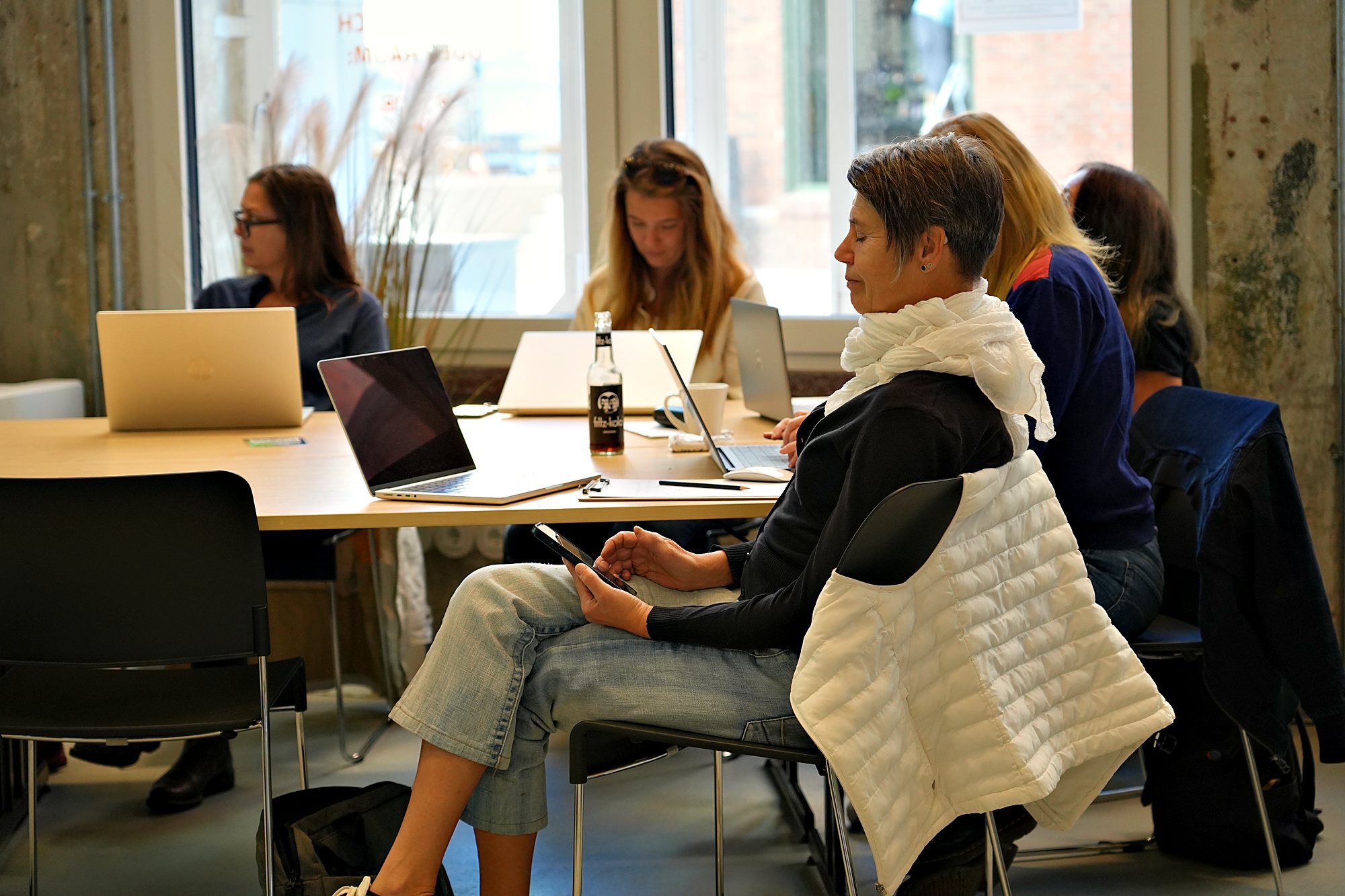 Teilnehmende arbeiten an Laptops am Tisch vor der Fensterfront