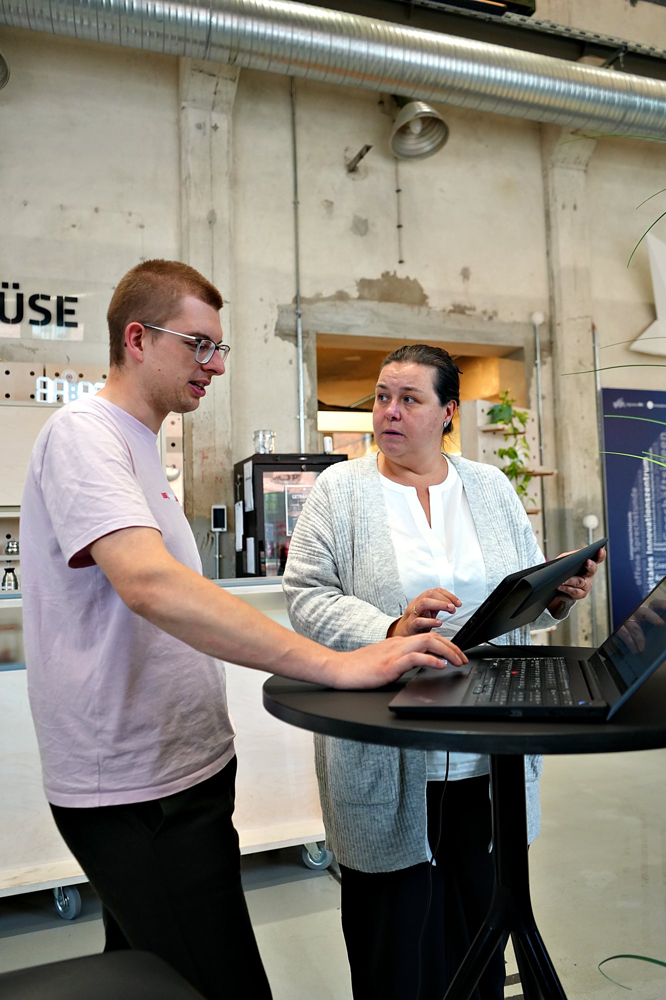 Ein junger Mann erklärt einer Teilnehmerin etwas am Stehtisch mit Laptop